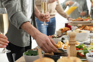 Man with glass of champagne taking food from buffet indoors, clo